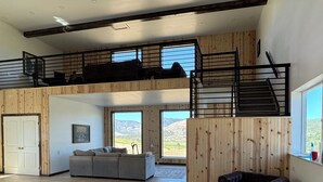 A spacious living area with a high ceiling, wooden beams, a sofa, a leather armchair, and a staircase leading to a loft.