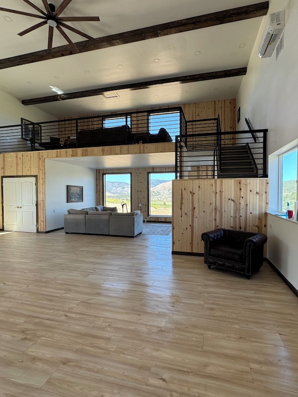 A spacious living area with a high ceiling, wooden beams, a sofa, a leather armchair, and a staircase leading to a loft.