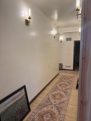Un pasillo con alfombra estampada, luces fijadas a la pared y un cuadro enmarcado.