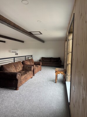 Een kamer met een bruine leren bank, een houten salontafel en een groot raam met houten jaloezieën.