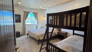 A room with two bunk beds, a window with curtains, a framed picture on the wall, and a door with a handle.