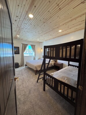 Una habitación con dos literas, una ventana con cortinas, un cuadro enmarcado en la pared y una puerta con pomo.