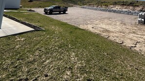 A gravel driveway leading to a building with a white exterior, a parked truck, and a clear blue sky.