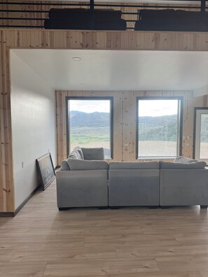 Een moderne woonkamer met een grote hoekbank, houten paneelwanden en grote ramen met uitzicht op een bergachtig landschap.