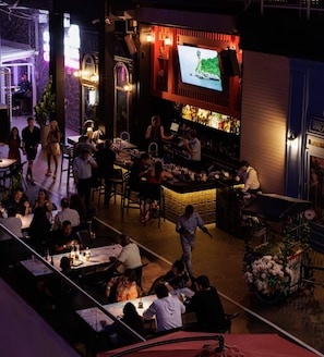 Una zona de bar con mesas, sillas, una pantalla de televisión y un camarero.