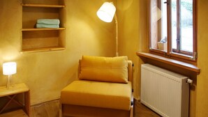 Une petite chambre agréable, dotée d’un lit simple, d’une lampe de chevet, d’une étagère avec des serviettes pliées et d’une fenêtre offrant une belle vue.