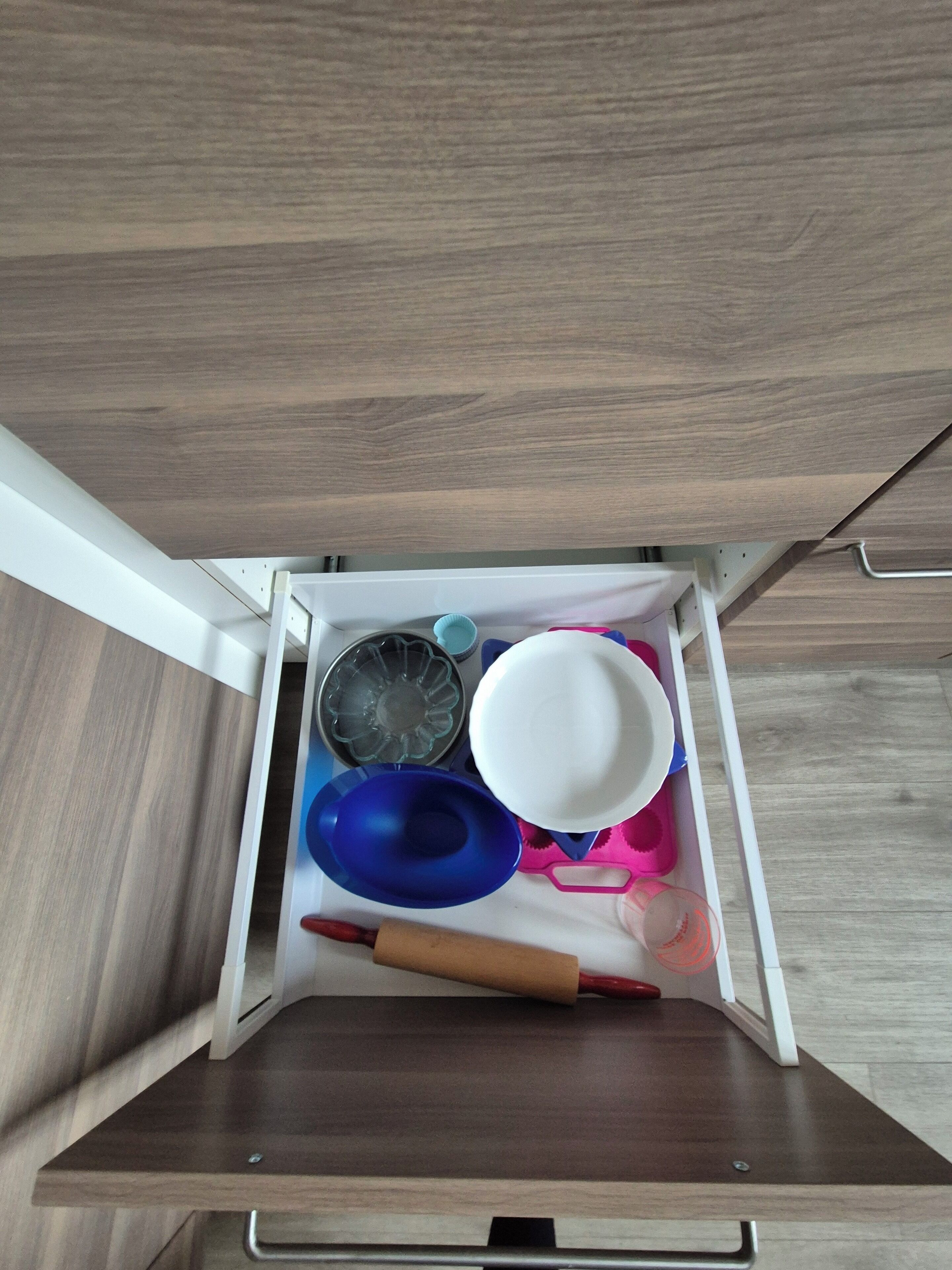 A drawer with various kitchen items including a rolling pin, bowls, and a glass container.