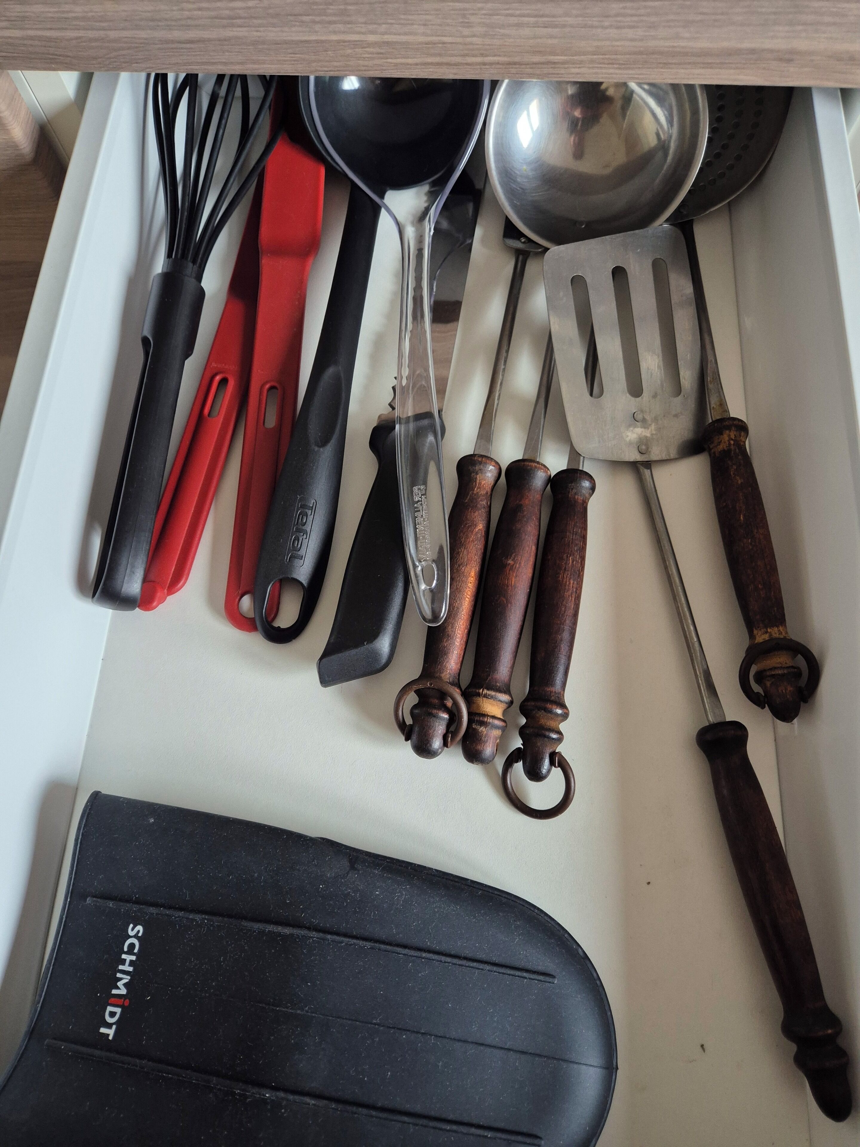 Uma gaveta com diversos utensílios de cozinha, incluindo batedores, uma colher, uma espátula e um suporte preto para facas SCHMIDT.