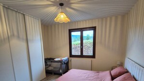 Ein Schlafzimmer mit Bett, Fenster, Heizkörper und Deckenleuchte.