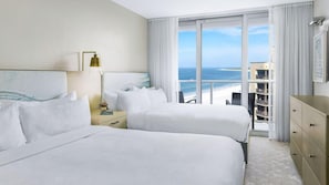 Habitación de hotel con dos camas, una mesita de noche, una lámpara, vista a la playa y un balcón con vista al océano.
