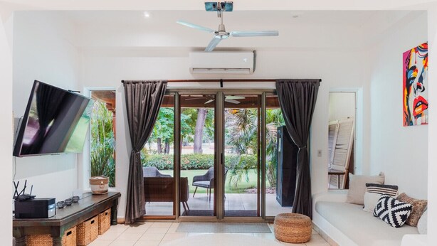 A modern living room with a flat-screen TV, a ceiling fan, a sofa, and a dining area with chairs. - Town House 4: Comfort and golf course view (Hacienda Iguana)