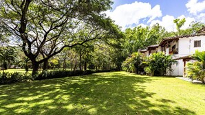 A well-maintained grassy area with a large tree and a building with a tiled roof. - Town House 4: Comfort and golf course view (Hacienda Iguana)