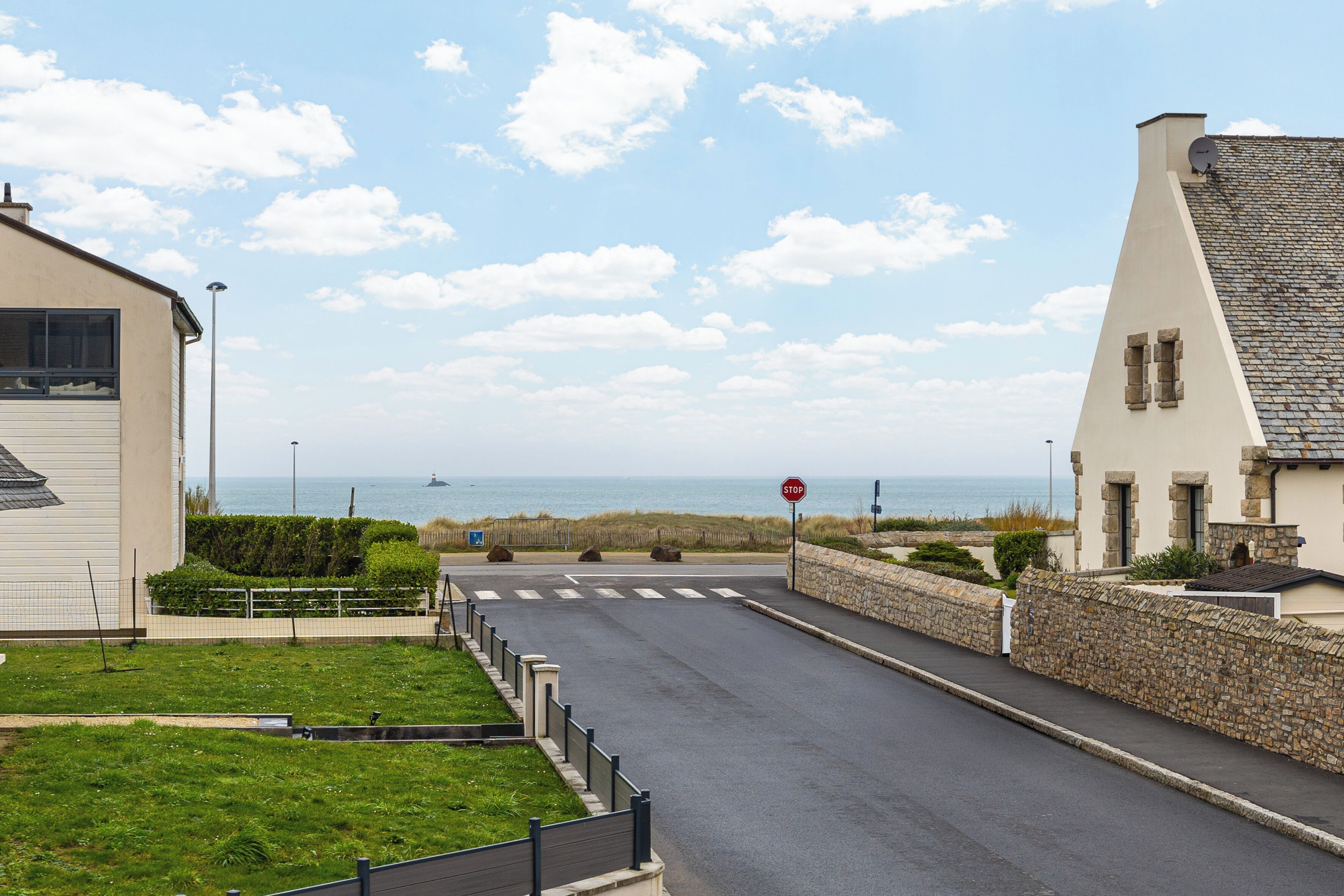 A coastal road with a stop sign, a stone wall, and a view of the sea.