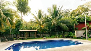 A swimming pool surrounded by lush greenery and a small pavilion. - Hotel Castillo Blanco (El Zonte)
