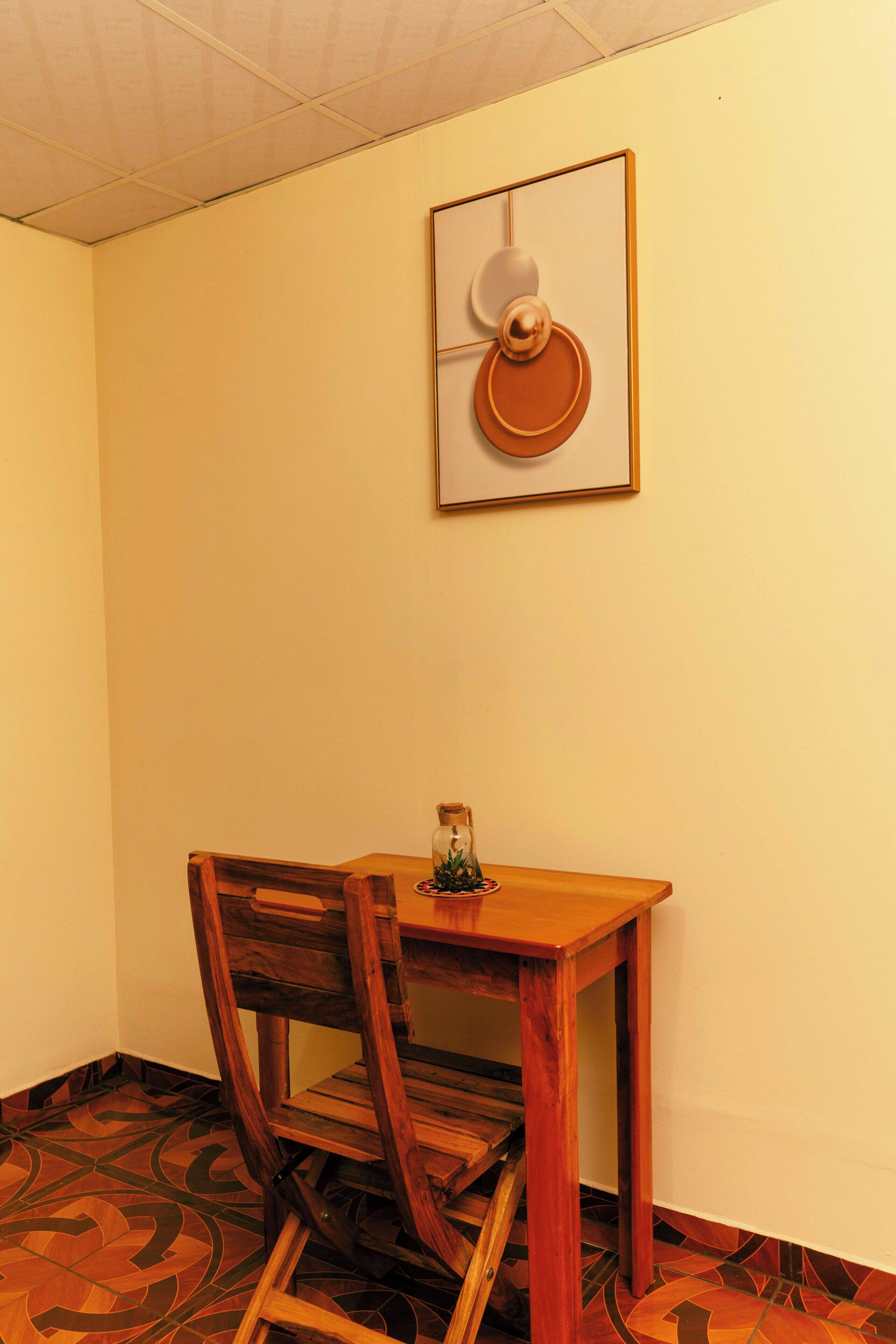 A corner room with a wooden table and chair, a framed artwork on the wall, and patterned floor tiles.