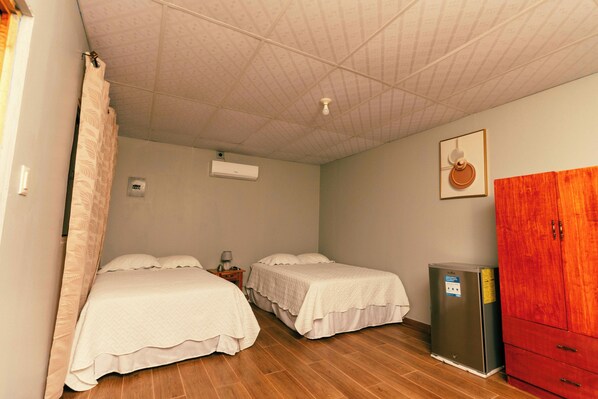 A room with two beds, a wooden floor, a red wardrobe, and a small refrigerator. - Hotel Castillo Blanco (El Zonte)