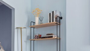 Un soggiorno moderno con un divano bianco, cuscini color verde acqua e arancioni, una lampada da terra alta e una libreria su una parete azzurra.