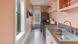 Una cucina piccola con un lavandino in acciaio inox, un frigorifero e un tostapane. Si vede una finestra sul lato sinistro e una porta che dà su un balcone.