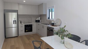 A modern kitchen with stainless steel appliances, white cabinetry, and a dining area with a white table and chairs.