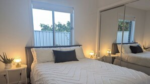 A bedroom with a large bed, two bedside tables with lamps, a window with a view, and a mirror on the wall.