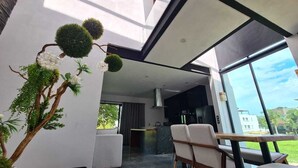 A modern interior with a dining area, a kitchen, and large windows offering a view of the outdoors. - Residence near the beach (Mezcales)