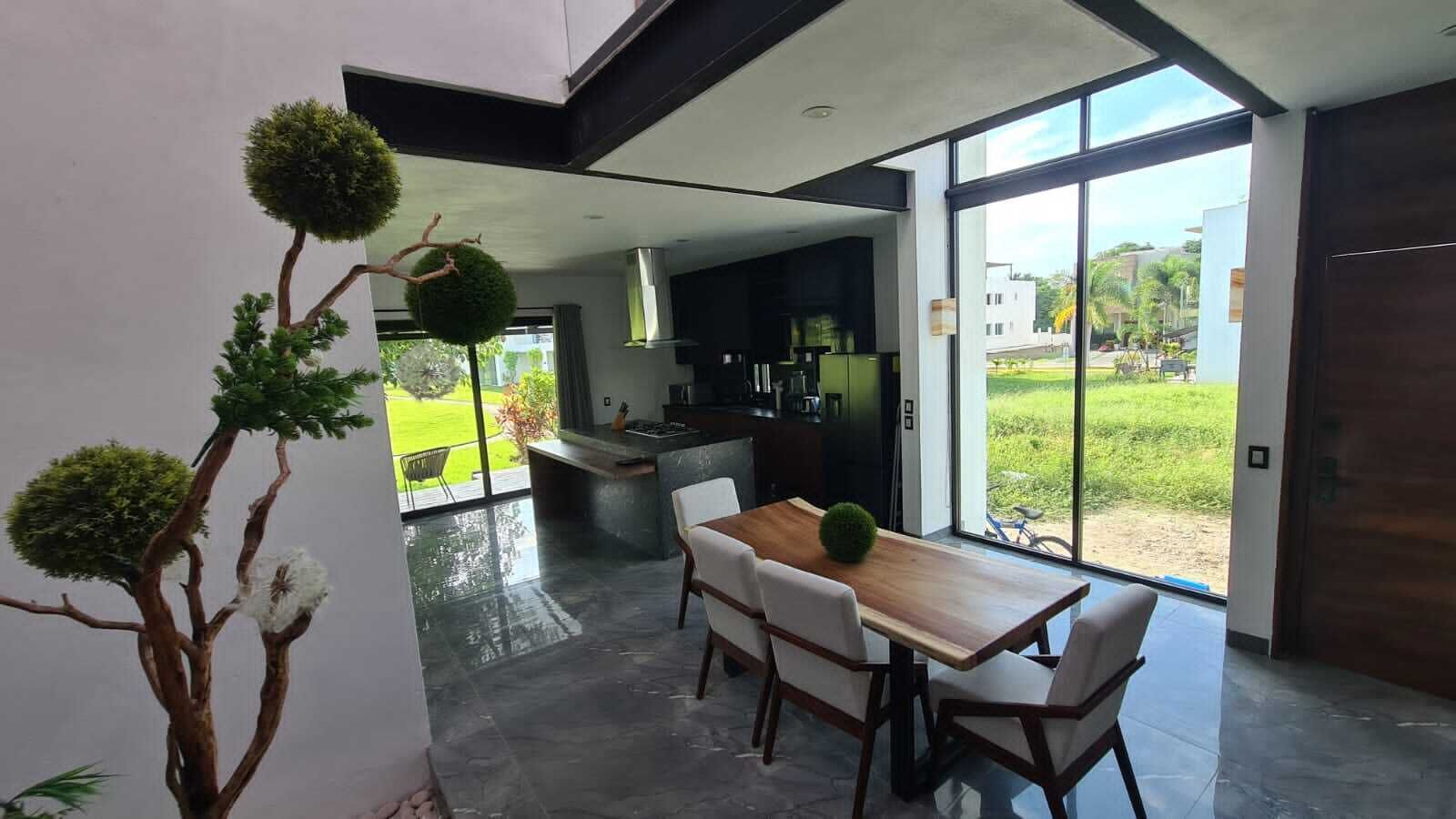 Een moderne keuken met een groot kookeiland, een eethoek met een houten tafel en stoelen, en grote ramen met uitzicht op de omgeving.