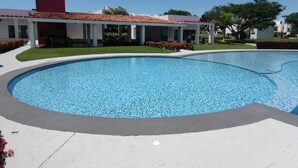 A swimming pool with a tiled deck, surrounded by a building with a red roof and white walls. - Residence near the beach (Mezcales)