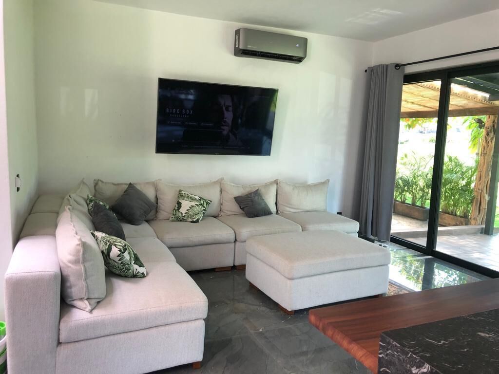 Una sala de estar moderna con un sofá modular, un televisor de pantalla plana montado en la pared y un ventanal corredizo que da a un área exterior.