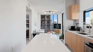 A modern kitchen with a central island, wooden cabinets, and a large window offering a city view. - Downtown Brickell - Desirable Location - We Host (Miami)