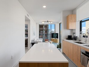 A modern kitchen with a central island, wooden cabinets, and a large window offering a city view. - Downtown Brickell - Desirable Location - We Host (Miami)