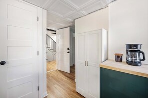 A hallway with white doors, a wooden floor, and a kitchen area with a coffee maker and a jar. - Mini Mews (Atlanta)