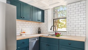Une cuisine moderne avec des armoires de couleur turquoise, un réfrigérateur en acier inoxydable et une fenêtre donnant sur les arbres.