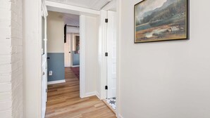 Un couloir doté d’un plancher en bois, de murs blancs et d’un tableau représentant un paysage, encadré.