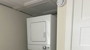 Une petite buanderie équipée d’un lave-linge et d’un sèche-linge à chargement frontal, d’un plan de travail en bois et d’une porte blanche.
