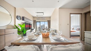 Une chambre d’hôtel moderne dotée d’un coin repas, d’une grande fenêtre offrant une vue sur la ville, d’un téléviseur à écran plat et d’un lit donnant sur le paysage urbain.