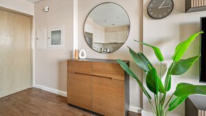 Une chambre d’hôtel moderne avec un plancher en bois, une armoire en bois, un miroir rond, une horloge murale et une plante en pot.