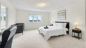 Ein Schlafzimmer mit einem großen Bett, einem Schreibtisch, einem Stuhl, einem Fenster mit Aussicht und einem Gemälde an der Wand.