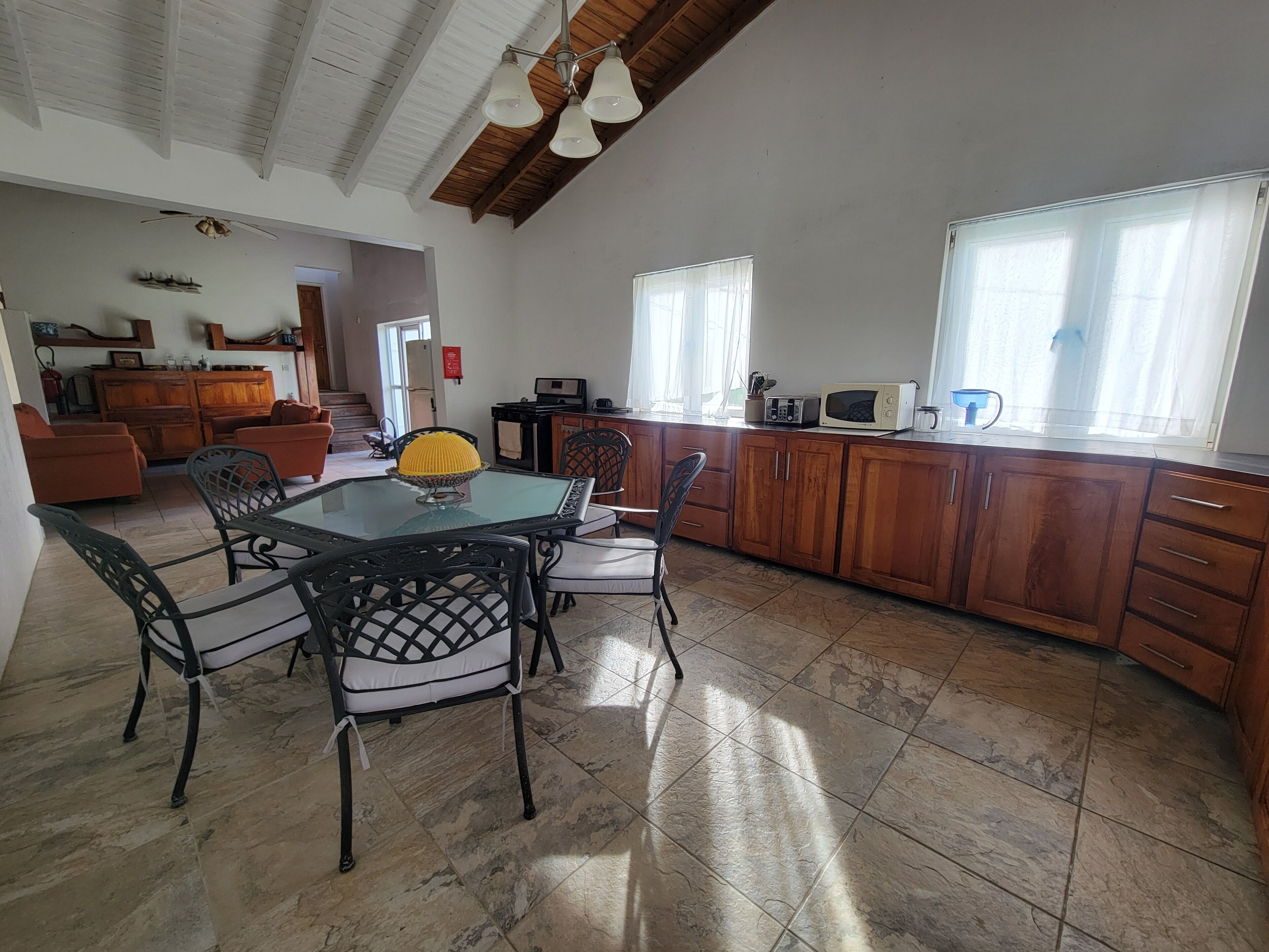 Un vaste espace de vie comprenant une table à manger avec un plateau en verre, des chaises noires et un bol décoratif jaune.