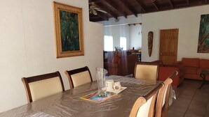 Un coin repas avec une table recouverte d’une feuille de plastique, des chaises en bois et un tableau accroché au mur.