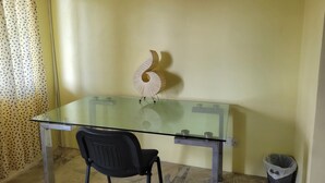 A small, simple room with a glass-top table, a black chair, a decorative wall piece, and a trash bin. - Spacious house located in Vieux Fort, few minutes from Hewanorra Airport (Vieux Fort)