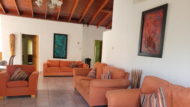 A spacious living area with orange sofas, a wooden ceiling, and two abstract paintings. - Spacious house located in Vieux Fort, few minutes from Hewanorra Airport (Vieux Fort)