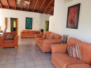 Ein großzügiger Wohnbereich mit orangefarbenen Sofas, einer Holzbalkendecke und zwei abstrakten Gemälden.