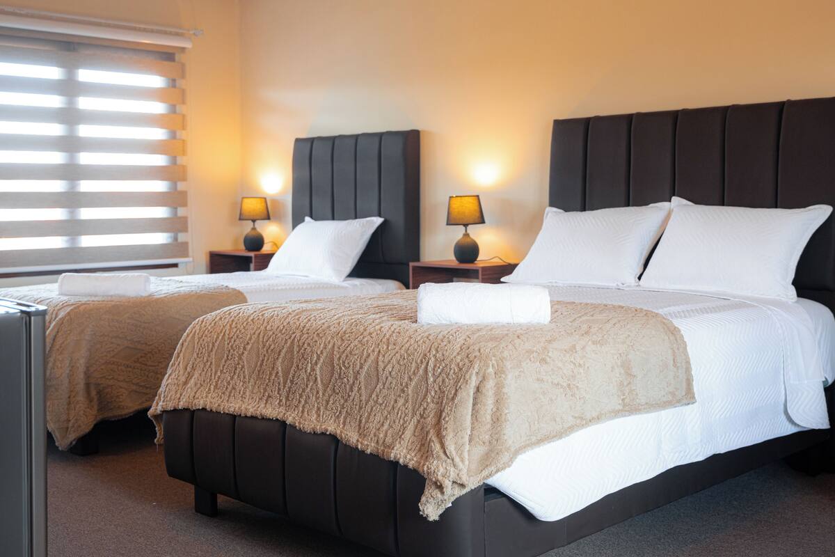 A double bed with a dark headboard, two bedside tables with lamps, and a window with blinds.