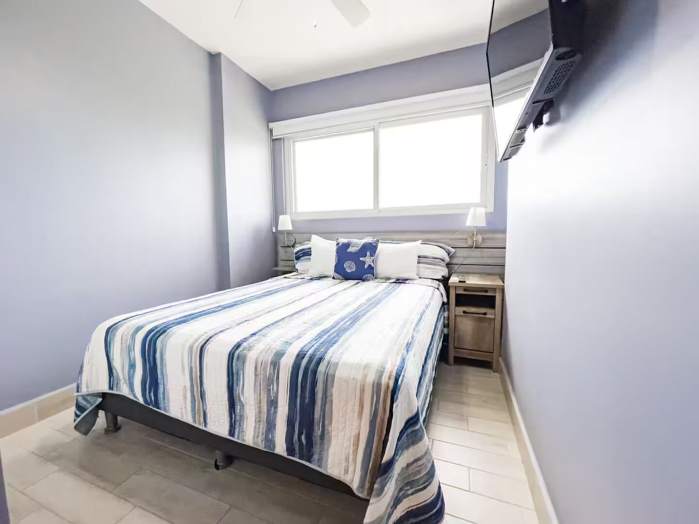 Une chambre à coucher avec un lit, des tables de chevet, une fenêtre et un ventilateur de plafond.