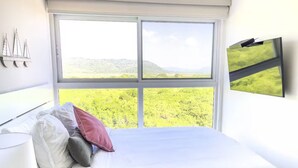 Una camera da letto con un'ampia finestra, un letto, un comodino e una televisione a schermo piatto montata a parete.