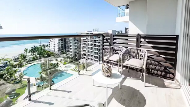 Un balcone con vista sulla spiaggia, una piscina e una zona pranzo con sedie e tavolo.