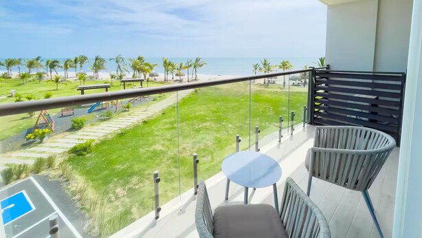 Un balcó amb vista a la platja, una piscina i mobiliari exterior.