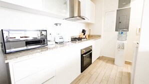 Cuina moderna amb armaris blancs, microones integrat, fogó i dispensador d'aigua.
