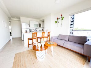 Ein modernes Wohnzimmer mit Essbereich, einem grauen Sofa und einer Küche im Hintergrund.