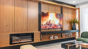 A modern living room with a large flat-screen TV mounted on a wooden wall, a built-in fireplace, and a comfortable seating area with a sofa and a coffee table. - Adventure Escape w Epic Themed Bedrooms Private Pool (Kissimmee)